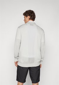 Light gray cardigan with a textured knit, featuring a subtle pattern and ribbed cuffs. Worn over black shorts, viewed from the back.