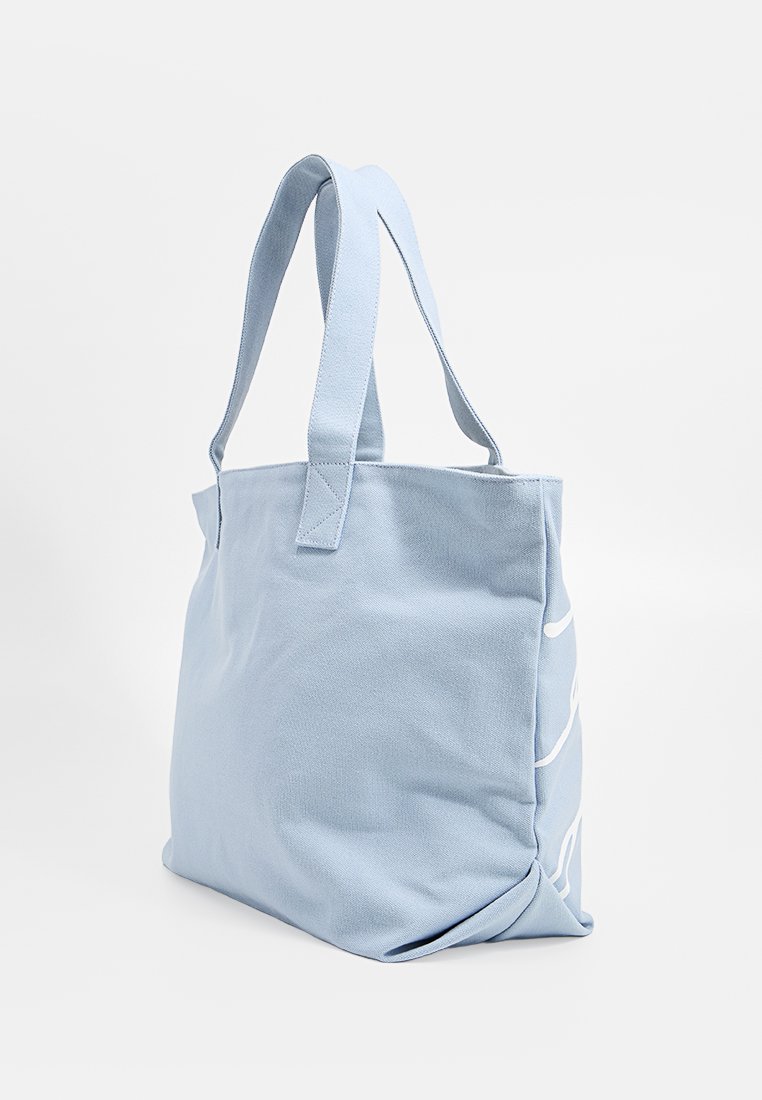 Helle blaue Canvas-Tote-Tasche mit breiten Tragegriffen und dezentem weißen Liniendesign an der Seite, auf weißem Hintergrund gezeigt.