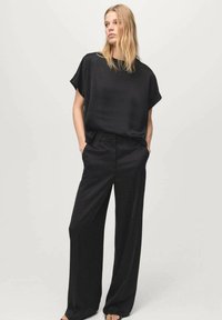 Czarny, luźny top z krótkim rękawem w połączeniu z czarnymi, szerokimi spodniami z wysokim stanem. Gładki materiał z minimalnymi detalami.