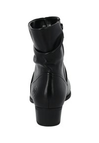 Botín de cuero negro hasta el tobillo con un diseño suelto en la parte superior, pequeño tacón, cremallera lateral y un acento de logo circular en la parte posterior. Textura suave.