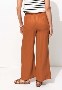 Pantalons larges en tissu couleur rouille avec une taille élastique ; associés à un haut rayé et des sandales à imprimé léopard brun.