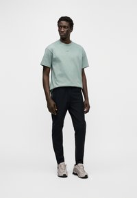 T-shirt de algodão verde claro com mangas curtas e um pequeno logotipo no peito, combinada com calças pretas e ténis cinza claro.