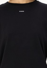 Μαύρο βαμβακερό μπλουζάκι με στρογγυλή λαιμόκοψη και κοντά μανίκια. Το όνομα της μάρκας "PINKO" εκτυπώνεται σε λευκό στο στήθος.