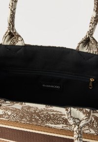 Nyitott barna és bézs mintás vászontáska, amely fekete belsőt mutat cipzáras zsebbel és az "even&odd" márkajelzéssel.