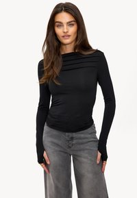 Zwarte longsleeve top met een gerimpeld ontwerp en gelaagde schouderdetails, gecombineerd met grijze wijde jeans. Soepele textuur, slim fit.