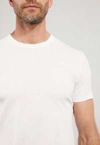 T-shirt blanc à col rond fabriqué en coton doux, avec des manches courtes et une coupe ajustée, adapté pour un usage décontracté.