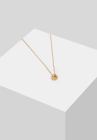 Guldkæde med en cirkulær vedhæng med intrikate designs og en lille rød ædelsten. Fin, delikat kæde. Elegant finish.
