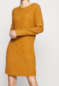 Robes en tricot côtelé de couleur jaune moutarde chaud. Dotée de manches longues, d'un col rond et d'une coupe légèrement cintrée à l'ourlet.