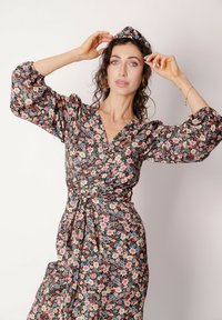 Kopertowa sukienka w kwiaty w kolorze czarnym z różowymi i niebieskimi kwiatami, z bufkami na rękawach, głębokim dekoltem w kształcie litery V oraz wiązanym paskiem w talii.