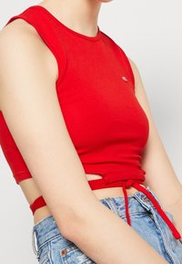 Top corto ajustado rojo hecho de algodón suave, con un escote redondo y un acento anudado en la cintura. Combinado con pantalones cortos de mezclilla de cintura alta.