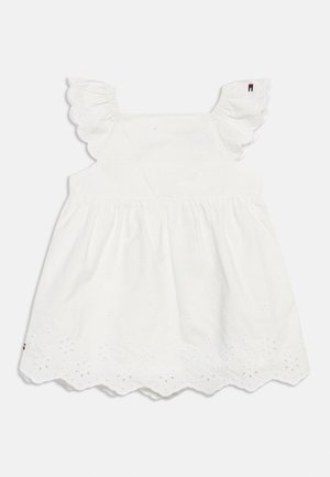 Robe blanche sans manches pour bébé avec broderie florale en œillet, ourlet festonné et bretelles à volants sur un fond uni.