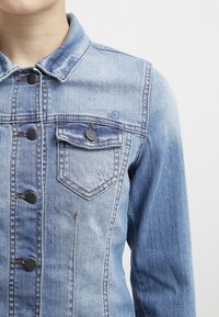 Ljusblå denimjacka med krage, knapprad framtill, två bröstfickor och subtila slitage detaljer på tyget.