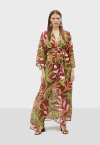 Robe longue et légère en brun avec un motif floral coloré en vert, rose et orange. Dotée de larges manches et d'une ceinture à nouer à la taille.