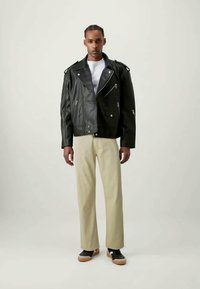 Black leather biker jacket with silver zip details, paired with beige trousers and black sneakers with beige accents.