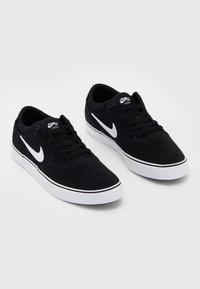 Czarne zamszowe sneakersy z białymi akcentami, z okrągłym czubkiem, płaską podeszwą i kontrastującymi czarnymi sznurówkami. Logo Nike wyeksponowane z boku.