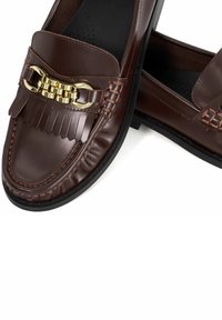 Brown leather loafers with a fringed design, gold-tone chain detail, black rubber sole, and smooth texture. Classic slip-on style.