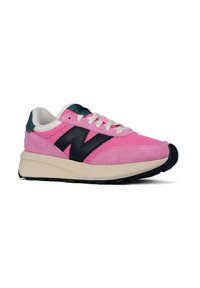 Pink and beige New Balance sneaker with black "N" logo, white laces, green heel tab, and black rubber sole, side view on white background.