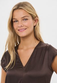 Smeđa bluzica s V-izrezom i kratkim rukavima, napravljena od glatkog materijala, s modernim dizajnom i suptilnim sjajem.