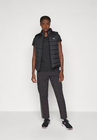 Vest cu puf negru cu guler înalt, asociat cu un tricou negru și pantaloni cargo negri. Adidașii au un accent roz și un design din plasă.