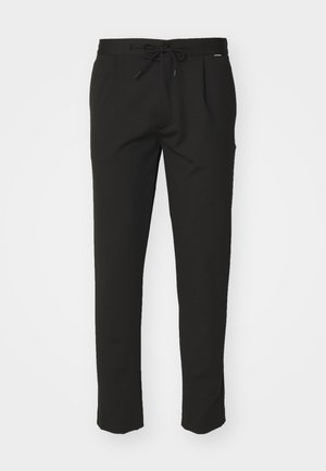 Svarte joggebukser med snøring i livet, to frontlommer, slim fit og et mykt, teksturert stoff. Ingen synlige logoer.