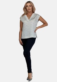 Biała bluzka w czarny prążkowany wzór, z dekoltem w kształcie V i krótkimi rękawami, w połączeniu z ciemnymi spodniami i metalicznymi szpilkami w wężowy wzór.