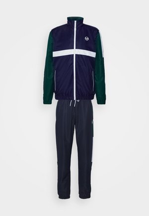 Compleu sport format dintr-o jachetă bleu marin cu accente albe și verzi, cu fermoar, și pantaloni asortați de culoare închisă, prevăzuți cu buzunare și manșete elastice.