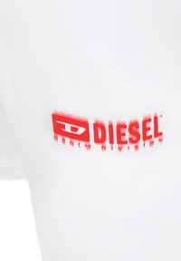 Pantaloni corti bianchi in cotone con un logo rosso "DIESEL" con effetto invecchiato. Texture morbida con una vestibilità rilassata e senza dettagli visibili.