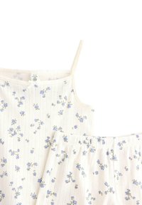 Setti vaalean kermanväristä pyjamapaitaa ja shortseja, joissa on pieniä sinisiä kukkakuosia, pehmeä tekstuuri ja säädettävät spagettiolkaimet.