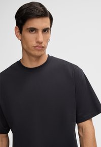 Zwarte katoenen T-shirt met een ronde hals, ruime pasvorm en korte mouwen. Soepele textuur met minimale naden en geen opvallende accenten.