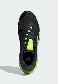 Zapatilla deportiva negra con parte superior de malla texturizada, detalles en verde lima y cordones negros. Cuenta con una suela resistente y un logo en la lengüeta.