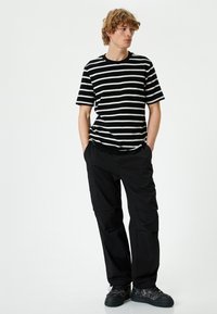 Sort og hvid stribet t-shirt med rund hals, parret med sorte cargo bukser med flere lommer og sorte sneakers.