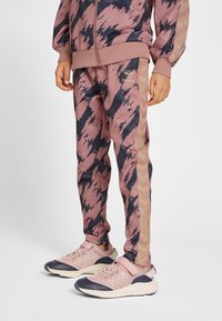 Mönstrad tracksuit i rosa och marinblått med en zip-up jacka och avsmalnande byxor med gulddetaljer och ränder. Bärs med rosa och marinblå sneakers.