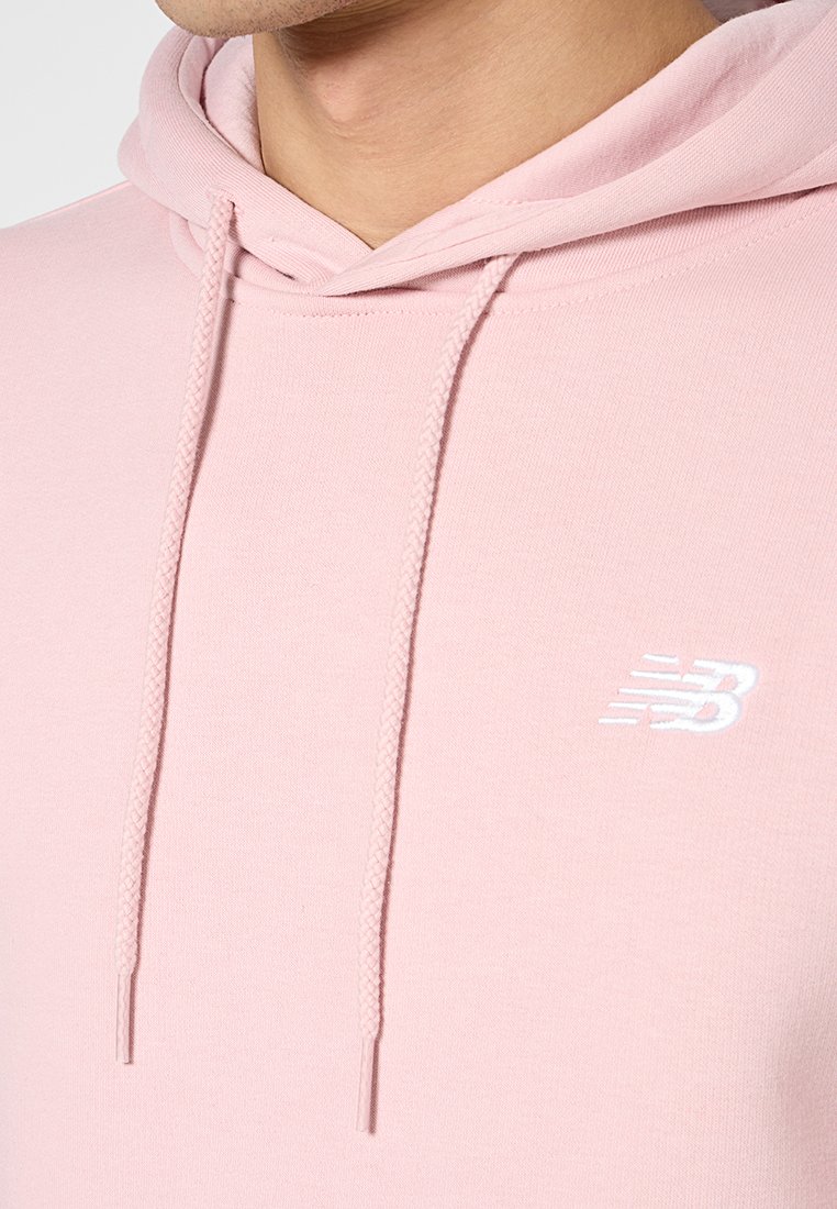 Sweatshirt rose avec une capuche à cordon, fabriqué à partir d'un tissu doux. Il présente un logo blanc sur la poitrine et une texture côtelée le long des bords.