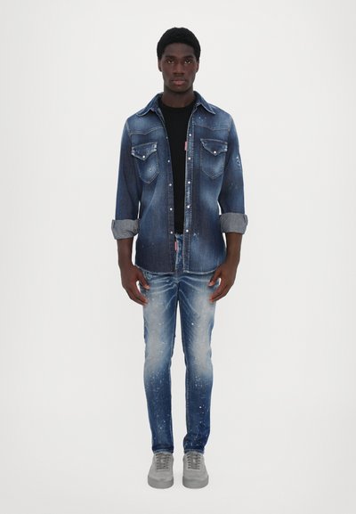 Denim shirt in light blue with distressed details, floral design, standard collar, and buttoned front. Paired with light blue jeans and gray sneakers.