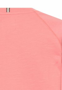 Hellrosa Sportoberteil aus strukturiertem Stoff. Mit Raglanärmeln, rundem Ausschnitt und sichtbaren Nähte-Details.