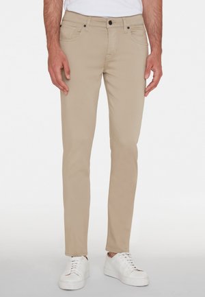 Beige Slim-Fit-Jeans aus einem Mischgewebe, ausgestattet mit vorderen und hinteren Taschen, Kontrastnähten und einem Knopfverschluss. Tragen mit weißen Sneakern.