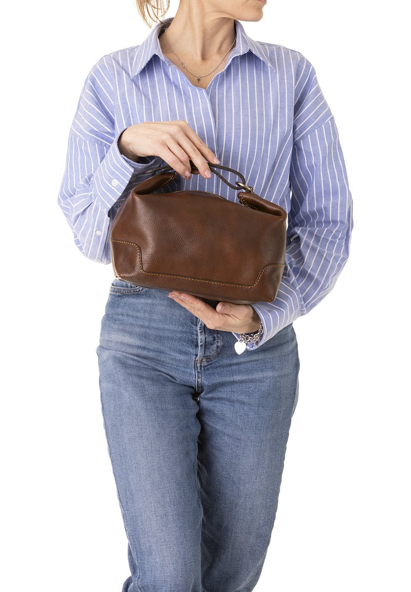 Bruine leren handtas met een ronde bovenkant, korte handvatten en zichtbare stikdetails. Vastgehouden voor een persoon in een gestreepte shirt.