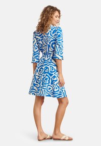 Kurzes Kleid mit kurzen Ärmeln in blau-weißer abstrakter Musterung, mit schmaler Taille und ausgestelltem Rock, aus glattem Stoff hergestellt, getragen mit leichten Sandalen.
