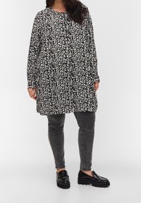 Robe à motifs floraux noir et blanc avec manches longues et encolure ronde, associée à un jean gris et des mocassins noirs.