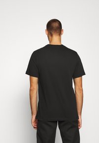 Svart bomullströja med standard rund halsringning, korta ärmar och rak nederkant. Enfärgad baksida, minimalistisk design, mjuk textur.