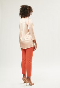 Helles rosa satin Bluse mit Dreiviertelärmeln, kombiniert mit engen orangen Hosen und beigen High-Heels. Glatte Textur, maßgeschneiderte Passform.