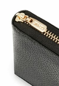 Zbliżenie rogu czarnego, textured skórzanego portfela z częściowo zamkniętym złotym zamkiem błyskawicznym na białym tle.