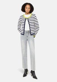 Granatowo-biały sweter w paski z limonkowym kołnierzem, zapinany na guziki, noszony na białej bluzce i jasnych dżinsach, uzupełniony czarnymi botkami na obcasie.