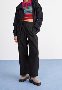 Pantalones cargo negros con cintura elástica, combinados con un suéter corto de rayas coloridas y botas grises con cordones y suelas gruesas.