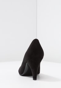 Zapato de tacón alto de ante negro con punta afilada y tacón esbelto. Textura suave y diseño simple sin adornos visibles.