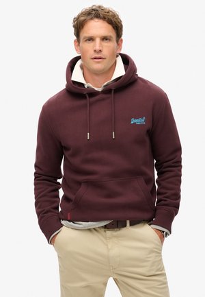 Bordeaux hoodie met een trekkoordkap en een voorkantoor, voorzien van een blauwe logo borduring. Gelaagd over een grijze shirt, gecombineerd met beige broek.