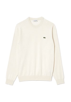 Suéter de cuello redondo color crema, con puños y dobladillo acanalados, que presenta un pequeño logo de cocodrilo bordado en verde en el pecho. Textura suave.