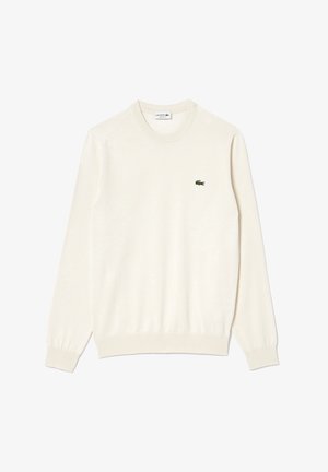 Kermanvärinen pyöreäkauluksinen villapaita, jossa on ribbireunat hihoissa ja helmassa, ja jossa on pieni vihreä brodeerattu krokotiililogo rinnassa. Pehmeä rakenne.