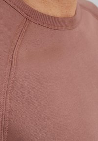 La camiseta de algodón en rosa empolvado presenta un cuello redondo, ribete acanalado y una textura suave con sutiles detalles de costura.