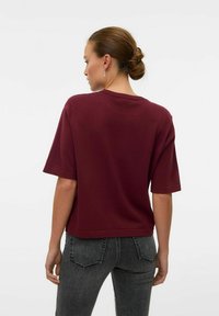 Top corto bordeaux a maniche corte con vestibilità rilassata, scollo arrotondato e tessuto testurizzato, abbinato a jeans alti grigi scuri.